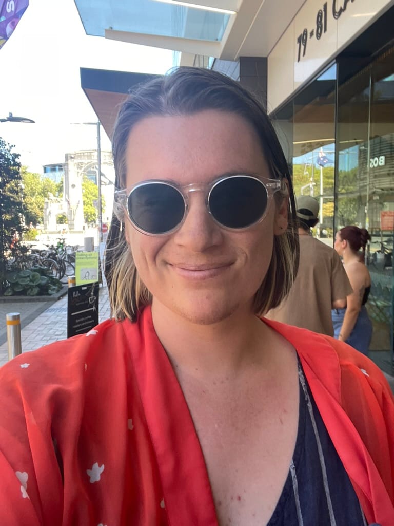 Me, a Pākehā femme, wearing a new pair of dark sunglasses and a bright orange shawl.